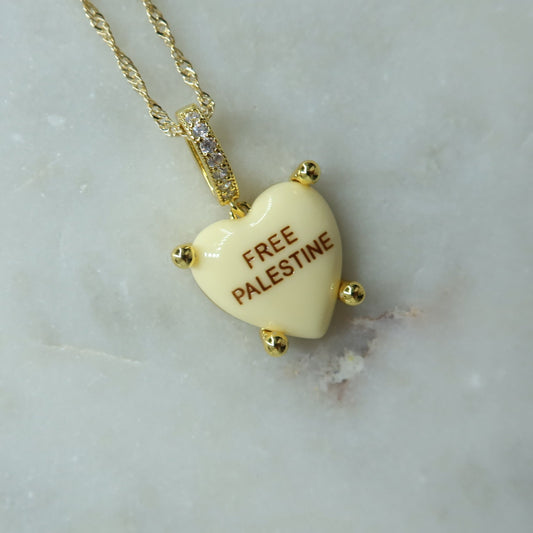 Heart-shaped pendant with 'Free Palestine' text on a gold chain against a marble background