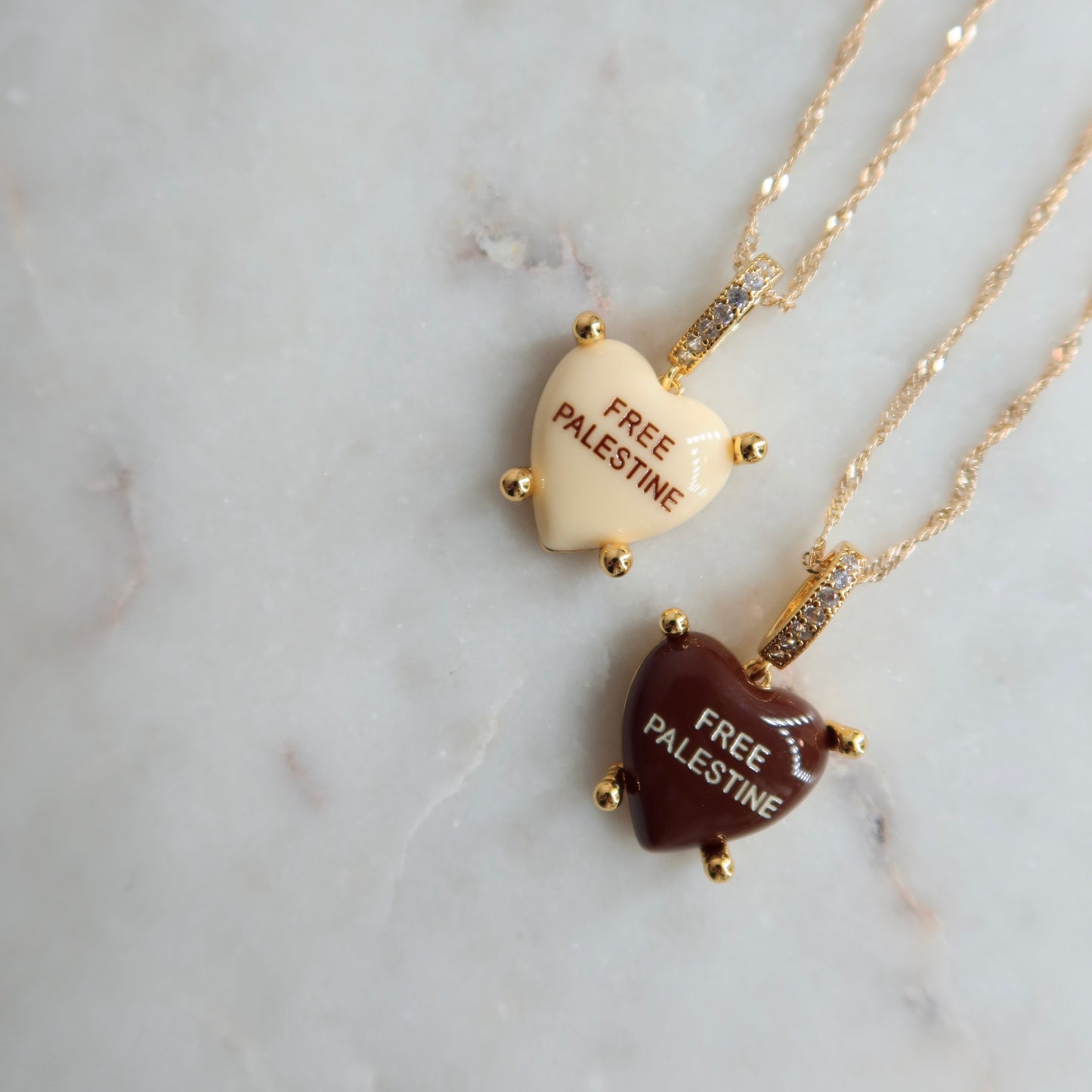 Two necklaces with heart-shaped pendants on a marble surface